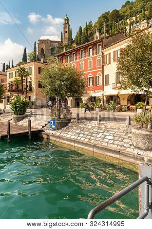 View Of Picturesque Village Morcote With Outdoor Bars And Gift Shops On The Shore Of Lake Lugano In