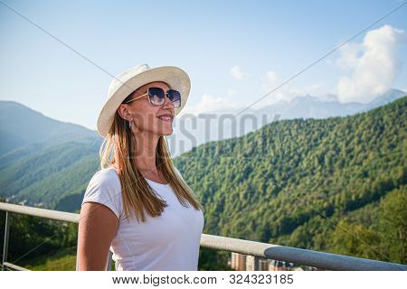 Girl Tourist In Glasses White Hat On The Background Of Mountains Looking Forward