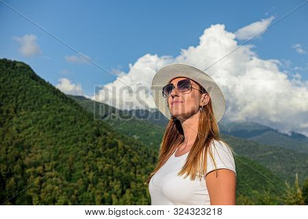 Girl Tourist In Glasses White Hat On The Background Of Mountains Looking Forward