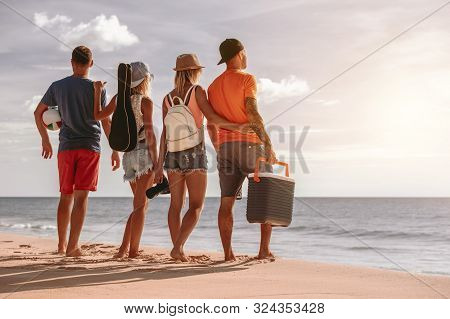 Four Friends Having Rest At Sunset Picknic On Sea Beach