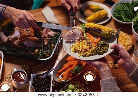 High angle view close up of the hands of a young mixed race man sitting at a table for Thanksgiving dinner at home carving the turkey and serving meat to a female friend holding her plate over the