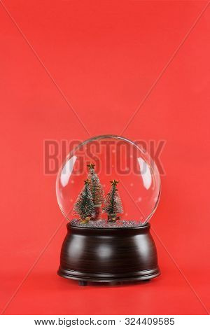 Christmas Snow Globe With Wooden Base And Bottle Brush Christmas Trees Against A Red Background. Fre