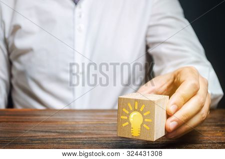 Businessman Holds A Wooden Block With An Image Of A Light Bulb Idea. Generation Of Innovative Busine