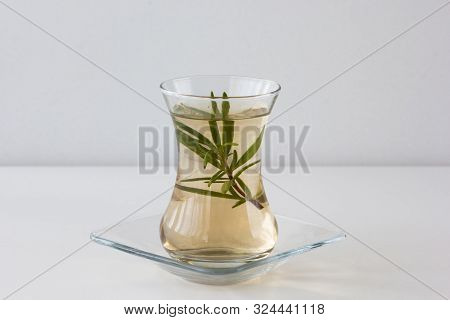 Rosemary Tea In Armudu Glass With Branch Of Rosemary In It On The Table On The White Background