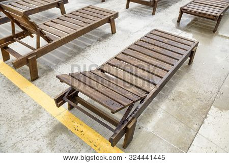 Row Of Empty Wooden Beach Chairs Near Water Outdoors.