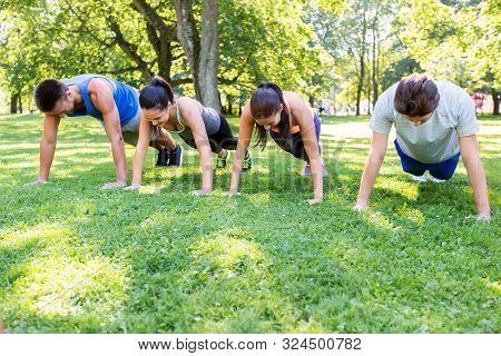 fitness, sport and healthy lifestyle concept - group of people doing push-ups or plank exercise at summer park or boot camp