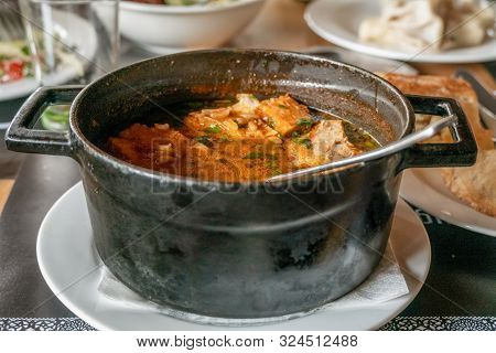 Kharcho Soup With Meat And Rice In A Cast-iron Bowl On A Wooden Table, Georgian Bread Is Next To It.