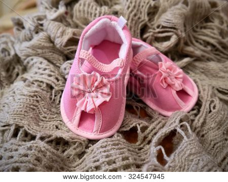 Baby Tiny Delicate Pink Booties With A Flower Bow. A Close-up Photo On The Background Of A Beige Sof