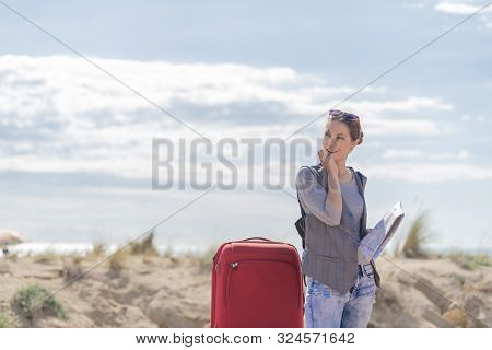 Young Blonde Holding A Map In One Of Her Hands While The Other Places It Serca Of The Mouth While Lo