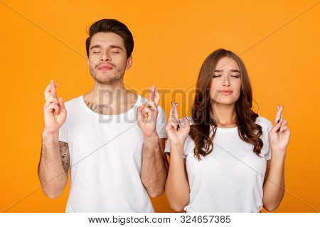Making Cherished Wish. Cheerful Couple With Closed Eyes And Crossed Fingers, Yellow Background
