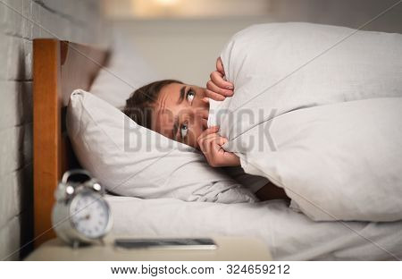 Anxiety And Insomnia. Anxious Girl Lying In Bed Being Afraid Pulling Blanket Over Face At Home At Ni