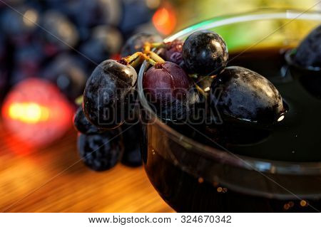 Glass Of Homemade Wine, Tincture Or Juice Next To Red And Black Grapes On A Background Of Multi-colo