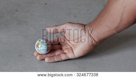 Small Globe On Hand With Grey Concrete Background Seen From The Side. World In Our Hands With Eniron