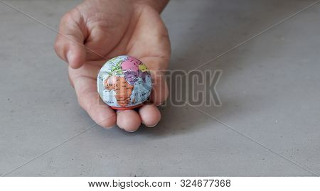 Small Globe On Hand With Grey Concrete Background Seen From The Front. World In Our Hands With Eniro