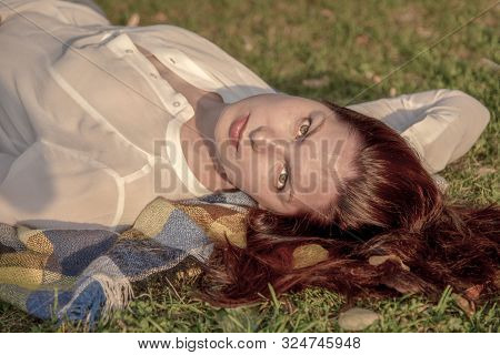 A 40-year-old Woman In A White Shirt Lies On A Plaid Blanket, On The Ground, Her Head To The Camera 