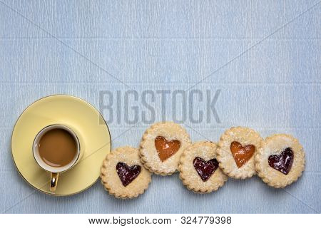 a row of jam heart biscuits with a cup of coffee on textured paper with a copy space, coffee break, dessert or love concept