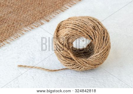 Natural Hemp Cord Ball And Burlap On A Rough White Surface. Roll Of Jute String Or Flax Twine. Coars