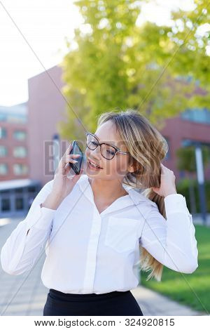 Smart Blonde Businesswoman Calling In Speakerphone Mode In Park