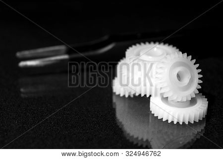 Several White Plastic Gears And Tweezers On A Black Mirror Background. Mechanical Repair. Fix. Refle