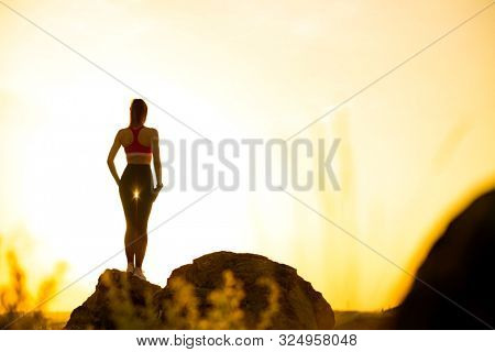 Young Beautiful Woman Standing on the Rock Against a Hot Beautiful Summer Sunset. Adventure and Healthy Active Lifesyle Concept.