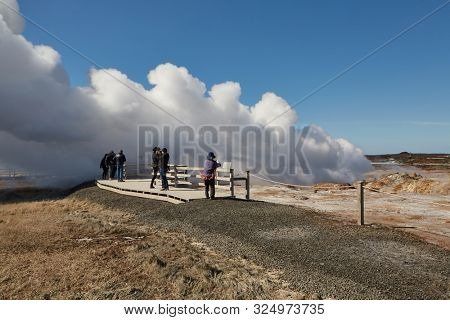 REYKJANES PENINSULA, ICELAND - APRIL 29, 2018: Steaming vents at Gunnuhver geothermal area in Iceland, viewing platform at a touristic lookout spot with tourists sightseeing