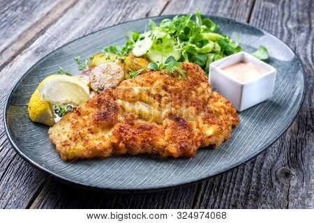 Fried Wiener schnitzel from veal topside with fried potatoes and lettuce as closeup modern design plate 