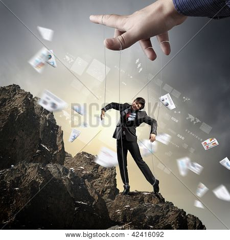 Marionete de empresário em cordas controlado pelo marionetista de pé no topo da montanha