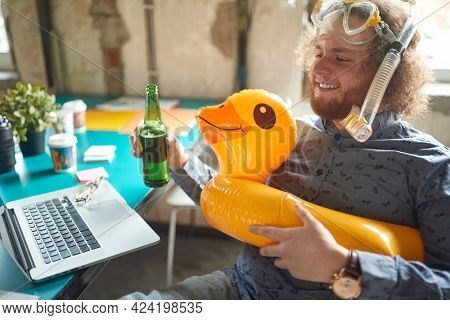 A young male office worker sitting in a relaxed atmopshere on the workplace and looking forward a vacation while imagining a beautiful beach. Employees, office, work