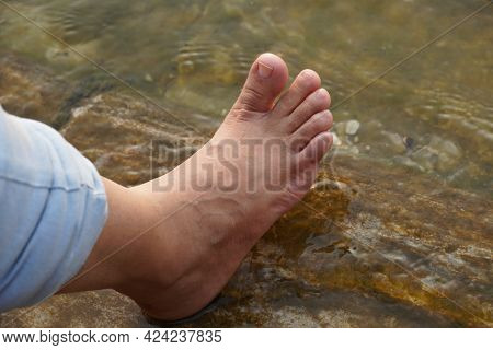 Female Feet In Running Water. Close-up Of Female Legs Wearing Jeans And Resting While Wetting Her Fe