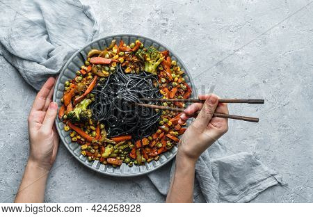 Hands Holding A Plate Of Black Spaghetti Or Pasta With Grilled Vegetables, Broccoli, Corn, Green Pea