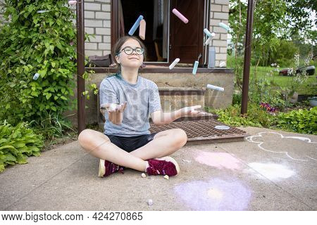 A Teenage Girl In Glasses With Multi-colored Hair Sits On The Porch Of The House And Draws On The Pa