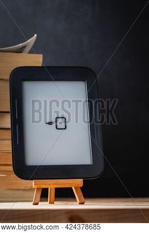 E-book Reader On The Wooden Stand Next To The Stack Of Paper Books At The Black Background.