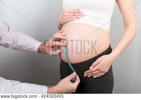 Happy Beautiful Pregnant Young Woman Touching Her Bare Tummy While A Doctor Is Measuring It