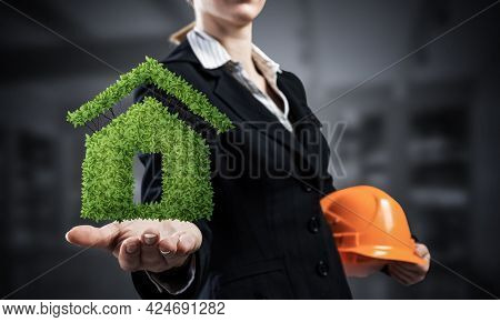 Real Estate Agent Holds In Palm Green Plant In Shape Of House. Woman In Business Suit With Safety He