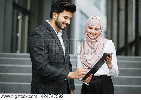 Side View Of Successful Arab Businessman Signing Papers On Clipboard That Holding Charming Woman In 