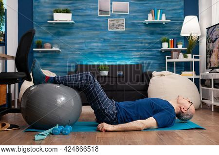 Retired Senior Sportman Sitting On Yoga Mat Practicing Warming Legs Up Exercises Using Swiss Ball St