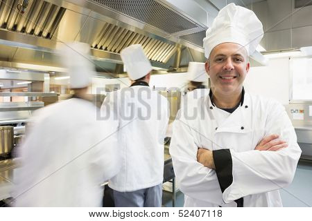 Head chef posing proudly in kitchen with colleagues in the background