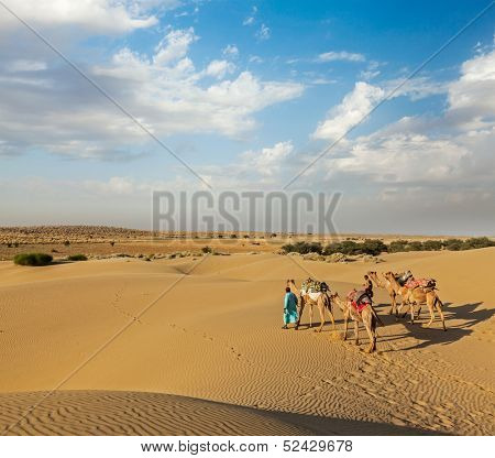 Rajasthan travel background - two Indian cameleers (camel drivers) with camels in dunes of Thar desert. Jaisalmer, Rajasthan, India