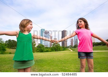 Two sister girls friends playing holding hand in urban modern skyline on park lawn
