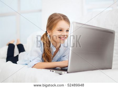 education, free time, technology and internet concept - little student girl with laptop pc at home