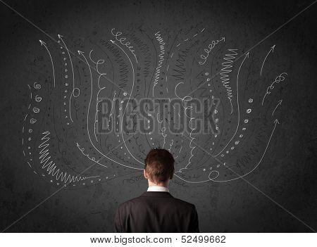 Thoughtful young businessman standing and deciding in front of a chalkboard with sketched arrows and lines in different directions