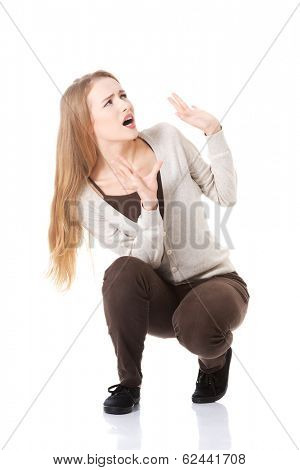 Beautiful casual woman is crouching from sth heavy above her. Isolated on white.