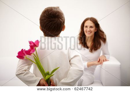 Rear view of lad with bunch of beautiful tulips behind back preparing nice surprise for his mother