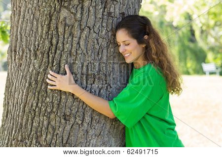 Beautiful young environmentalist embracing tree trunk in park