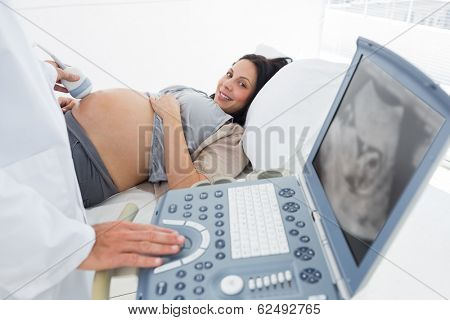 Midsection of male doctor operating ultrasound machine with pregnant woman in background