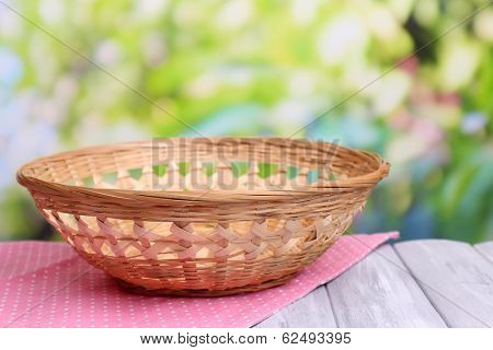Empty wicker basket on wooden table, on bright background