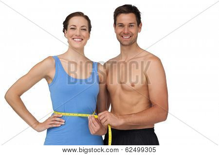 Portrait of a fit young man measuring womans waist over white background