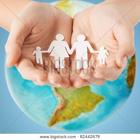 people, population, charity and life concept - close up of human hands holding paper family over earth globe and blue background
