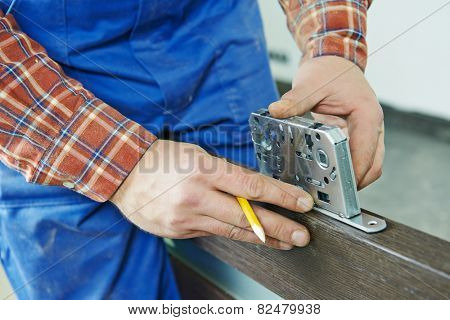 Close-up carpenter hands with doorlock during lock process installation into wood door