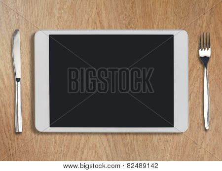 tablet pc looking like ipad on wooden table with fork and knife